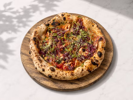 Pizza finished with red micro herbs on a wooden board in dappled daylight — shot on site by a Splento creator