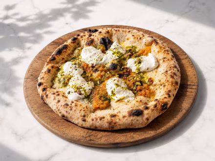 Pizza with pesto and burrata on a wooden board in dappled daylight — shot on site by a Splento creator