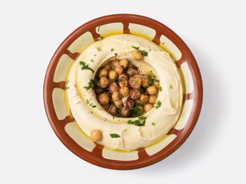 Bowl of hummus topped with chickpeas, olive oil and parsley, uploaded by a merchant and edited by Splento