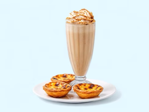 Biscuit milkshake under whipped cream beside three custard tarts, uploaded by a merchant and edited by Splento